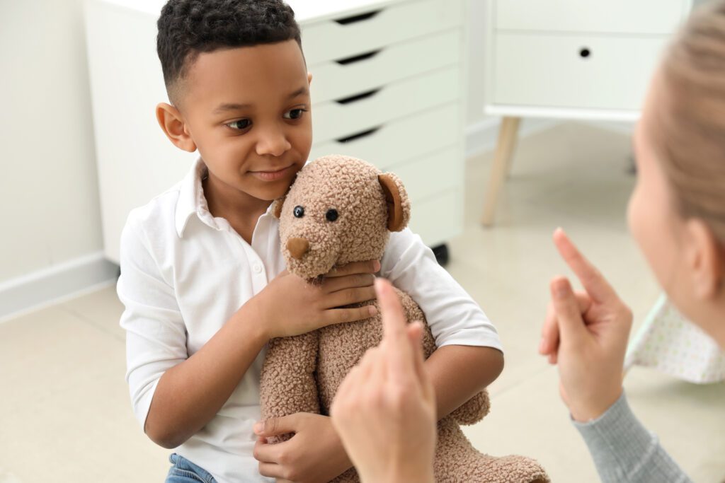 a speech language pathologist treating a little boy holding a teddy bear